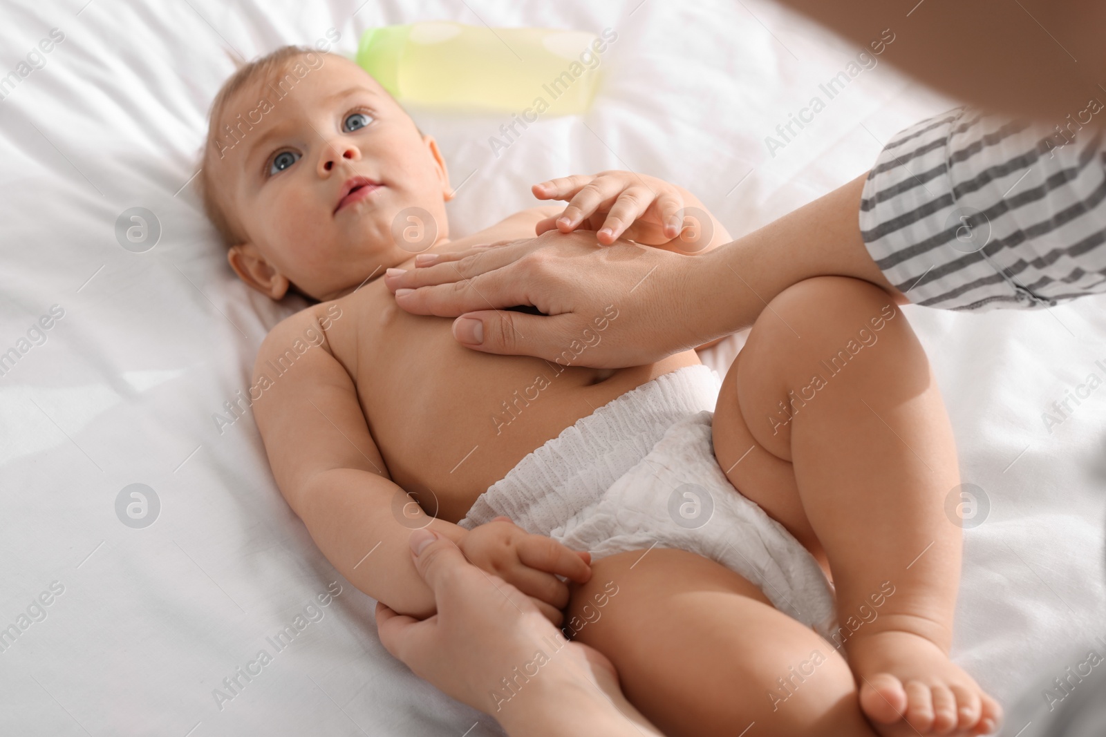 Photo of Mother massaging her cute baby with oil on bed