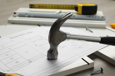 Photo of White furniture assembly parts, plan and hammer on wooden table, closeup