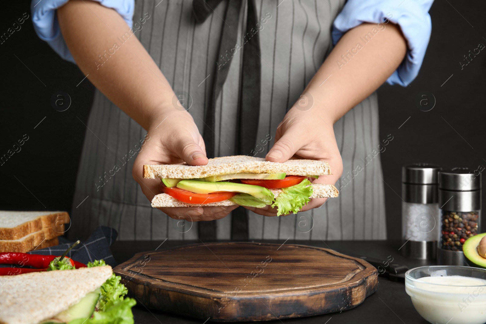 Photo of Woman holding tasty sandwich at black table, closeup