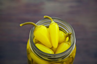 Glass jar of pickled yellow jalapeno peppers on wooden table, closeup