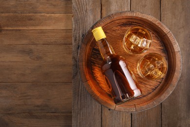 Whiskey with ice cubes in glasses, bottle and barrel on wooden table, top view. Space for text