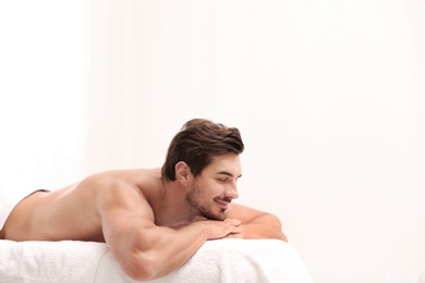 Photo of Handsome young man relaxing on massage table against light background, space for text. Spa salon