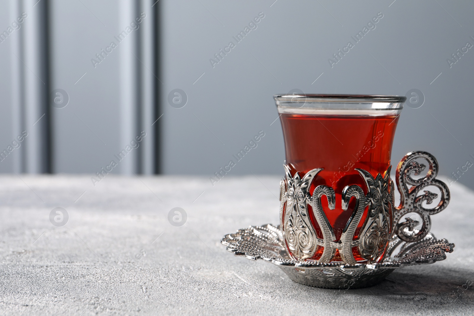 Photo of Glass of traditional Turkish tea in vintage holder on light grey table. Space for text
