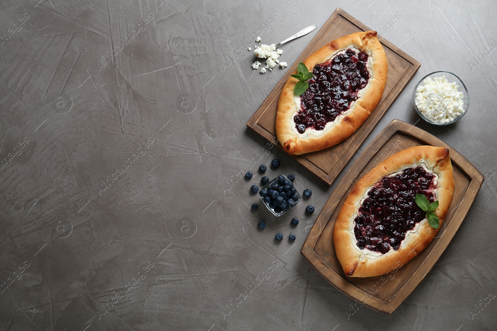 Photo of Delicious sweet cottage cheese pastry with cherry jam and fresh blueberries on grey table, flat lay. Space for text