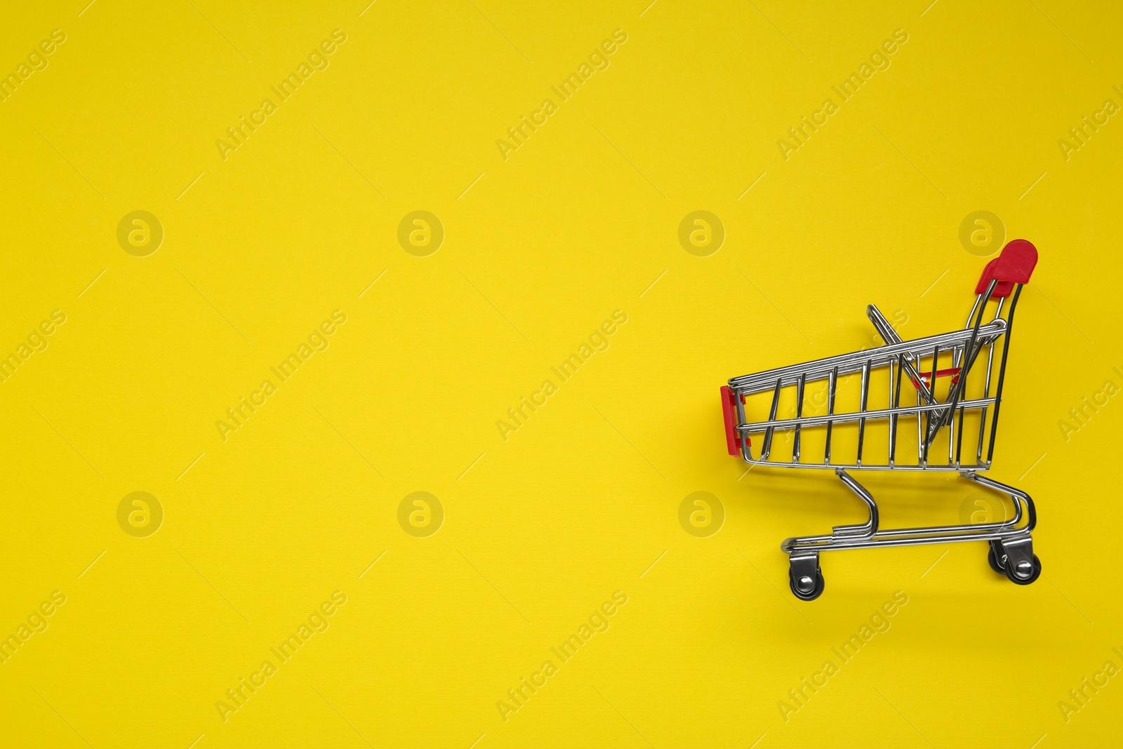 Photo of Small metal shopping cart on yellow background, top view. Space for text