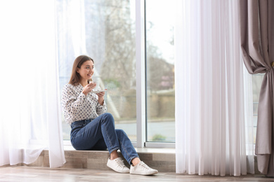 Photo of Young woman with cup near window indoors