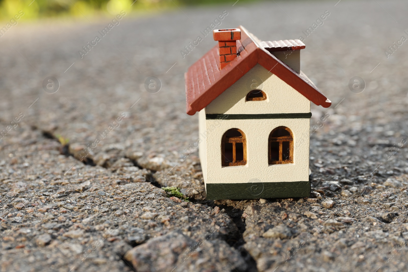 Photo of Wooden house model on cracked asphalt. Earthquake disaster