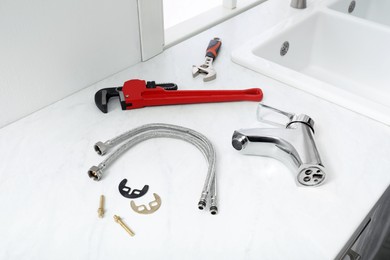 Photo of Parts of water tap and wrenches on white marble countertop in kitchen