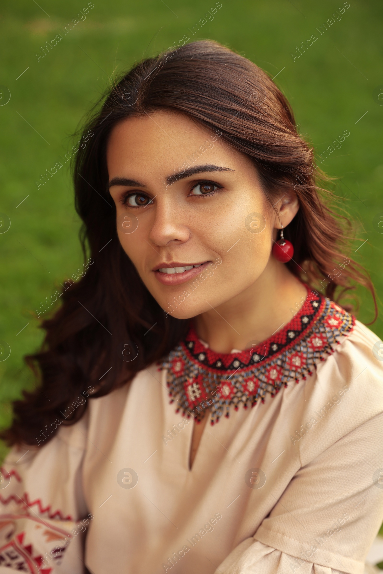 Photo of Beautiful woman wearing ornate beaded necklace and red earrings outdoors. Ukrainian national jewelry