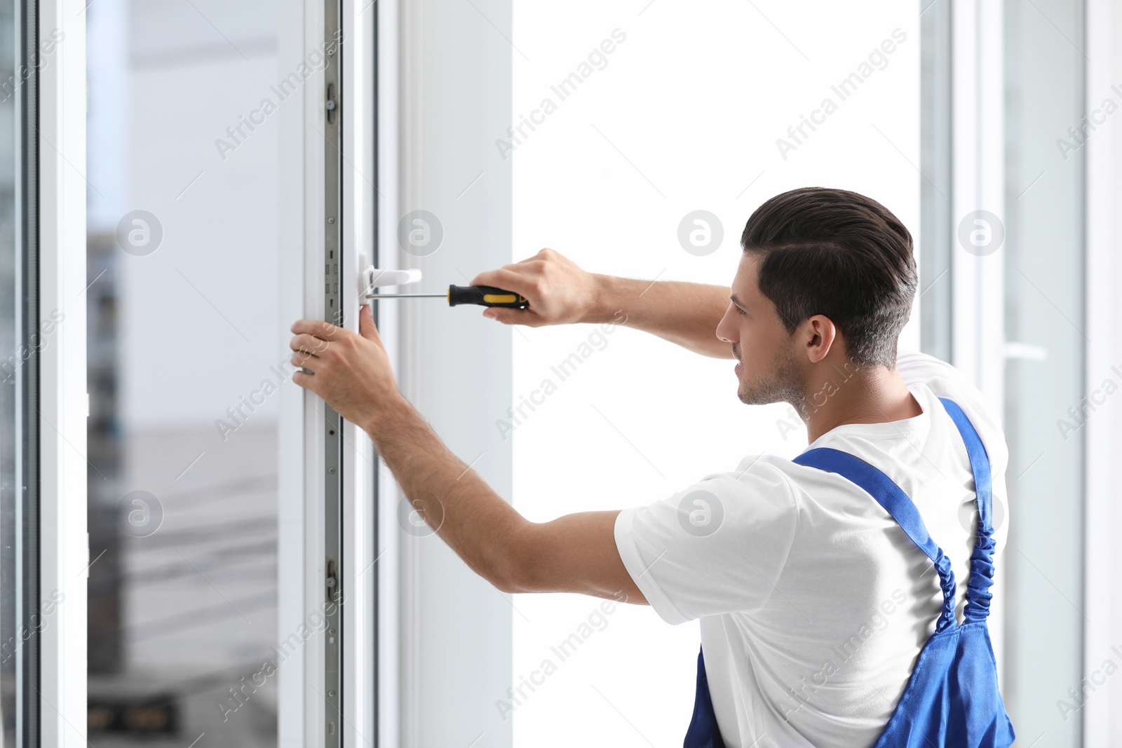 Photo of Construction worker repairing plastic window with screwdriver indoors