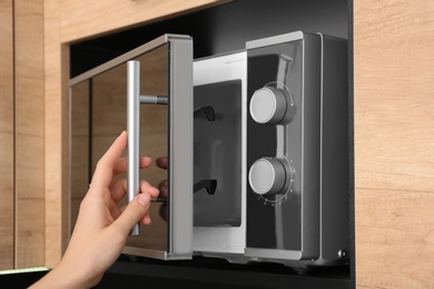 Young woman using microwave oven in kitchen, closeup