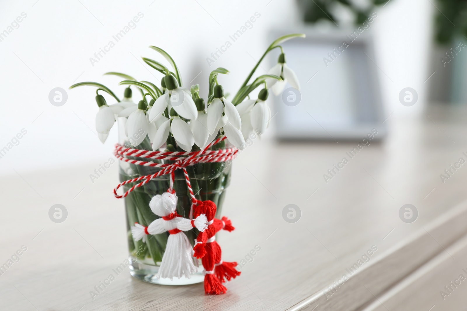 Photo of Beautiful snowdrops with traditional martisor on table indoors, space for text. Symbol of first spring day