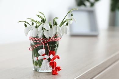 Photo of Beautiful snowdrops with traditional martisor on table indoors, space for text. Symbol of first spring day