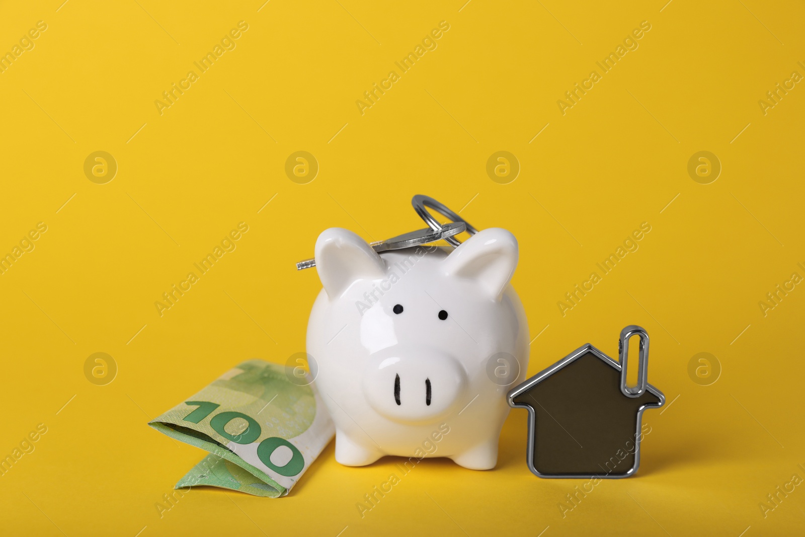 Photo of Ceramic piggy bank, euro banknote and key with trinket on yellow background. Financial savings