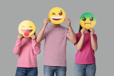 People covering faces with emoticons on grey background