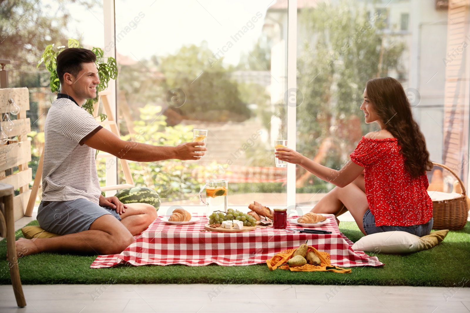 Photo of Happy couple with refreshing drinks imitating picnic at home