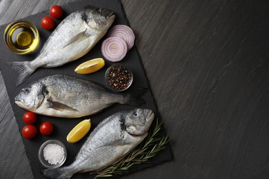 Photo of Fresh raw dorado fish, lemon, spices and tomatoes on black table, flat lay. Space for text