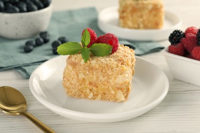 Photo of Piece of Napoleon cake with raspberries and spoon on wooden table, closeup
