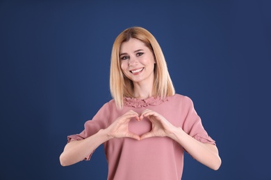 Portrait of woman making heart with her hands on color background