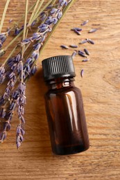 Bottle of essential oil and lavender flowers on wooden table, flat lay