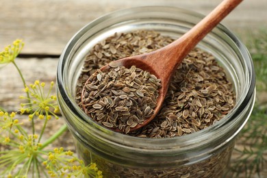 Jar with dry dill seeds and spoon on wooden table, closeup