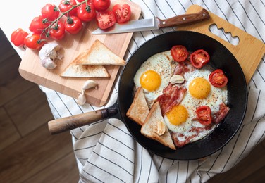 Delicious fried eggs with bacon and tomatoes in pan on table, flat lay