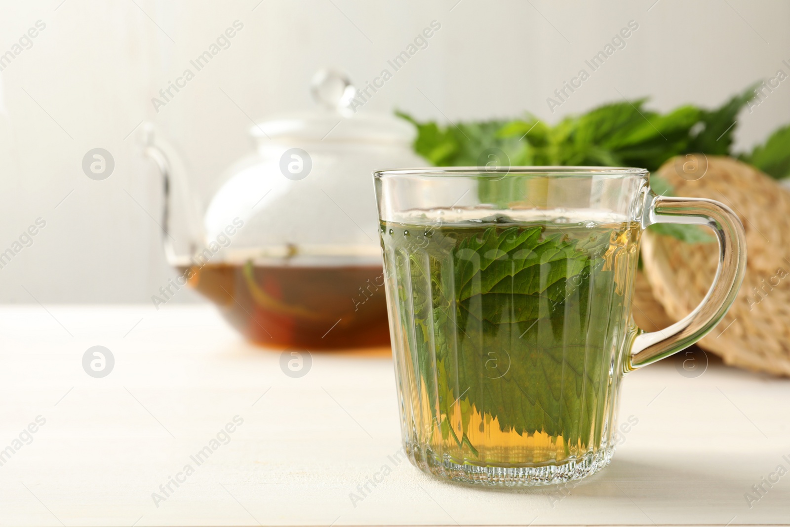 Photo of Glass cup of aromatic nettle tea on white wooden table, space for text