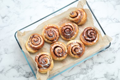 Photo of Baking dish with tasty cinnamon rolls on white marble table, top view