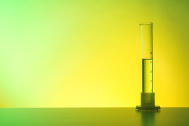 Photo of Graduated cylinder with liquid on table against color background. Chemistry laboratory glassware