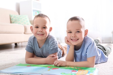Photo of Portrait of cute twin brothers with book on floor in living room