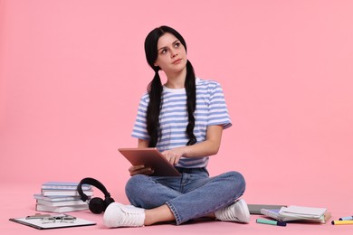 Photo of Student with tablet sitting among books and stationery on pink background
