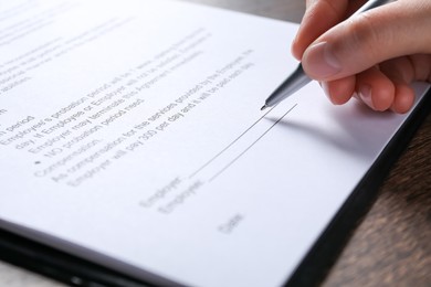 Photo of Woman signing document with pen at wooden table, closeup