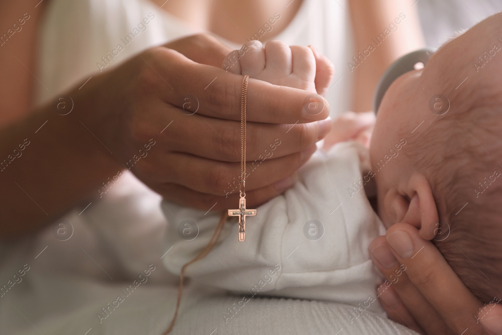 Photo of Mother holding Christian cross near newborn baby indoors, closeup