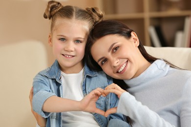 Little girl and her mother making heart with hands indoors