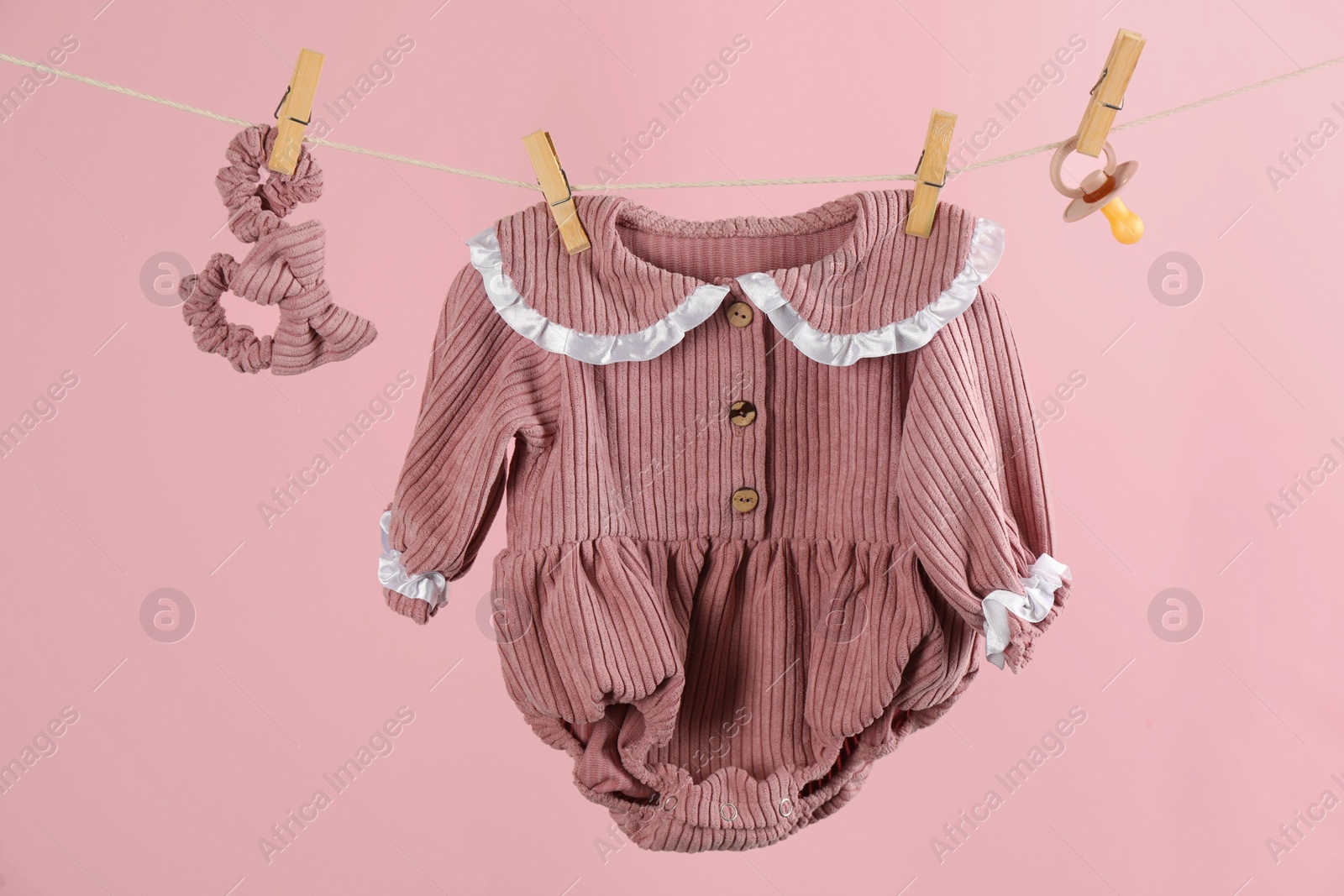 Photo of Baby clothes and accessories hanging on washing line against pink background