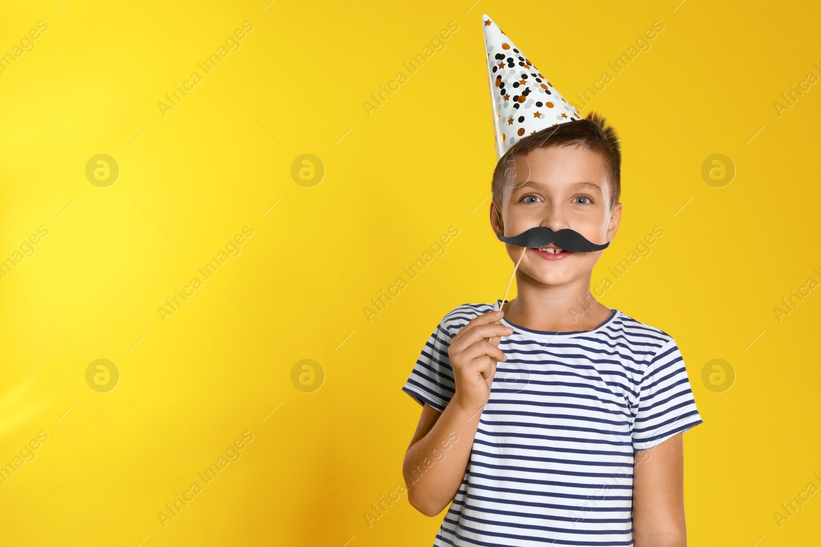 Photo of Little boy with photo booth props on yellow background, space for text. Birthday celebration