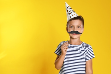 Photo of Little boy with photo booth props on yellow background, space for text. Birthday celebration