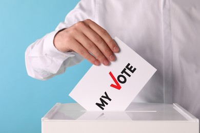 Man putting paper with text My Vote and tick into ballot box on light blue background