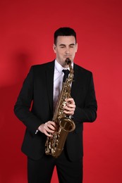 Photo of Young man in elegant suit playing saxophone on red background