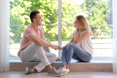 Photo of Happy young couple sitting near window at home
