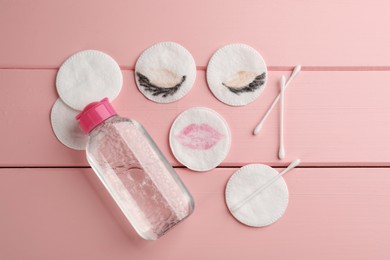 Photo of Dirty cotton pads, swabs and micellar cleansing water on pink wooden background, flat lay