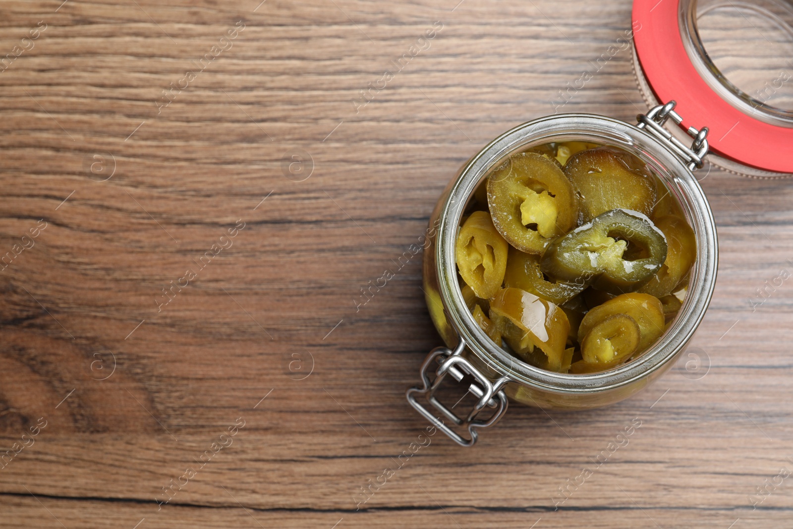 Photo of Glass jar with slices of pickled green jalapeno peppers on wooden table, top view. Space for text