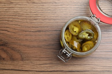 Photo of Glass jar with slices of pickled green jalapeno peppers on wooden table, top view. Space for text