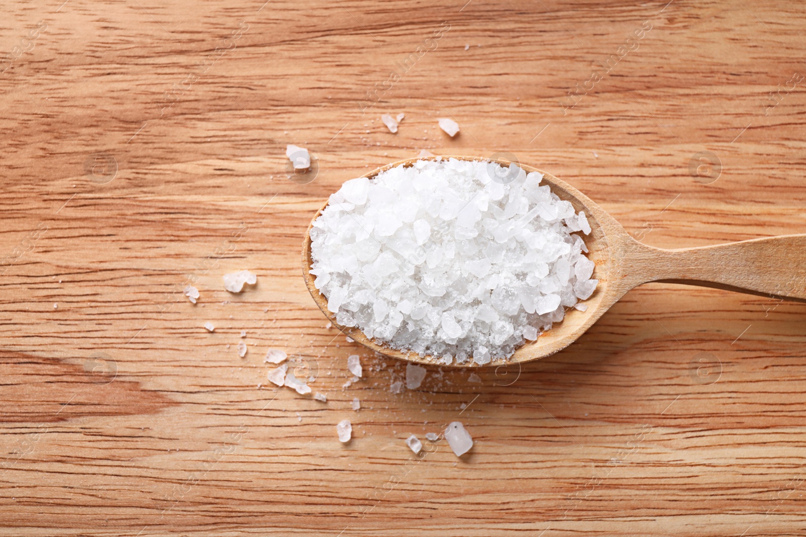 Photo of Spoon with white sea salt on wooden table, top view. Spa treatment