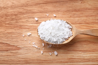 Photo of Spoon with white sea salt on wooden table, top view. Spa treatment