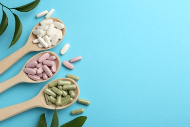 Different vitamin pills in spoons and green leaves on light blue background, flat lay. Space for text