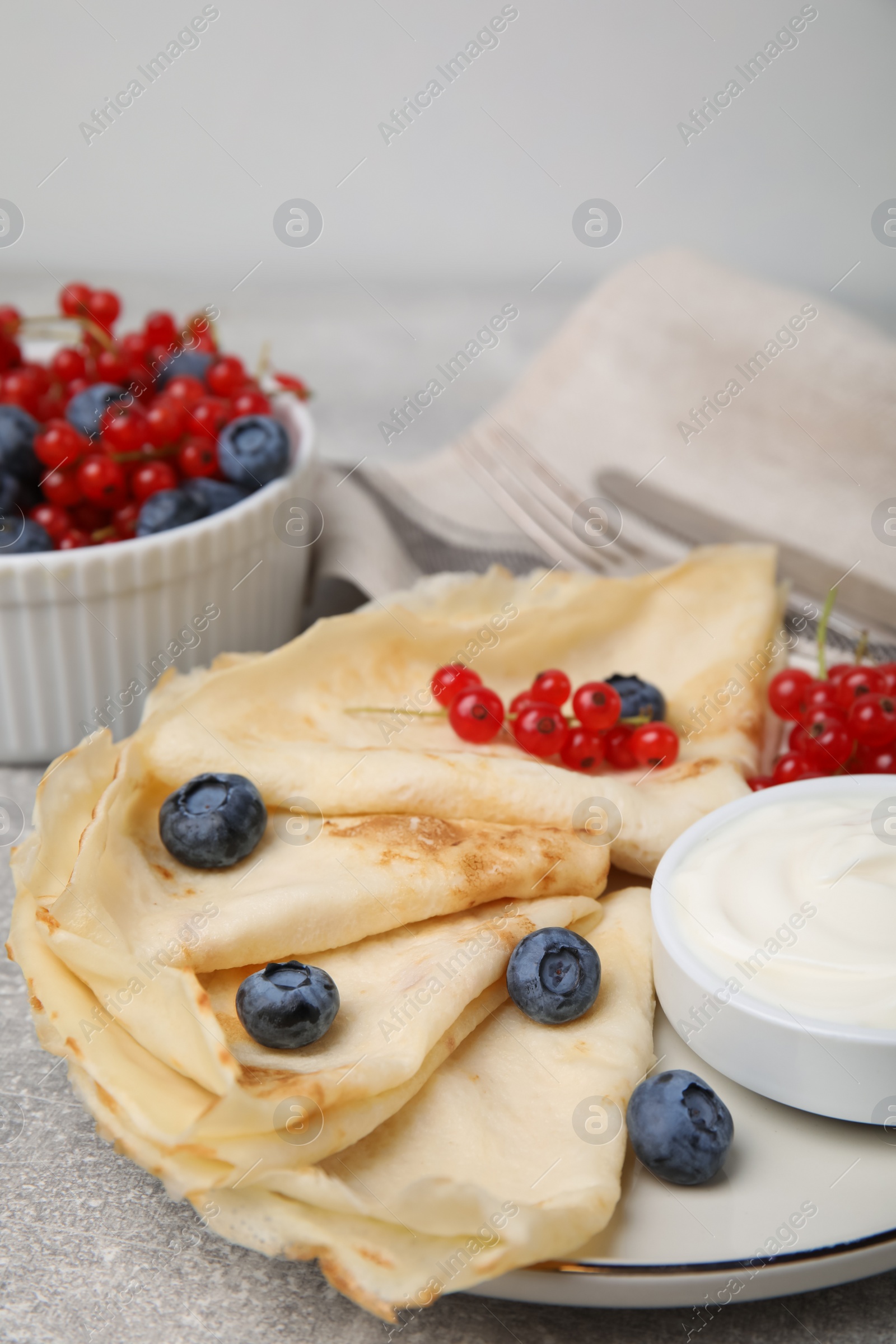 Photo of Delicious crepes with natural yogurt, blueberries and red currants on grey table. Space for text