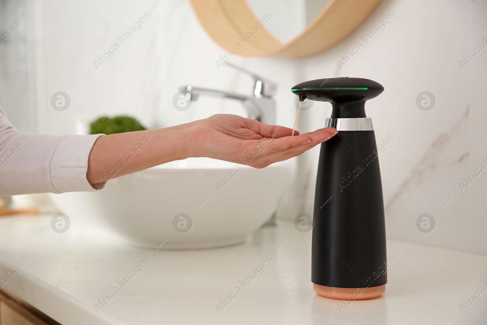 Photo of Woman using automatic soap dispenser in bathroom, closeup
