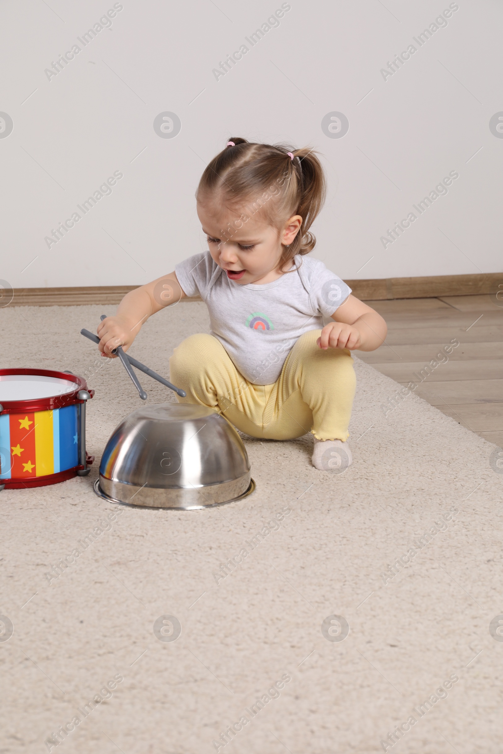 Photo of Cute little girl with cookware and toy drum at home