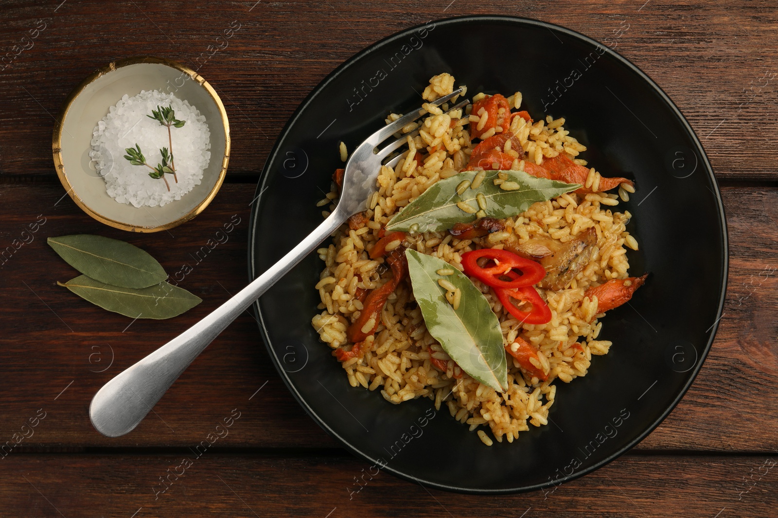 Photo of Delicious pilaf, bay leaves, fork and salt on wooden table, flat lay